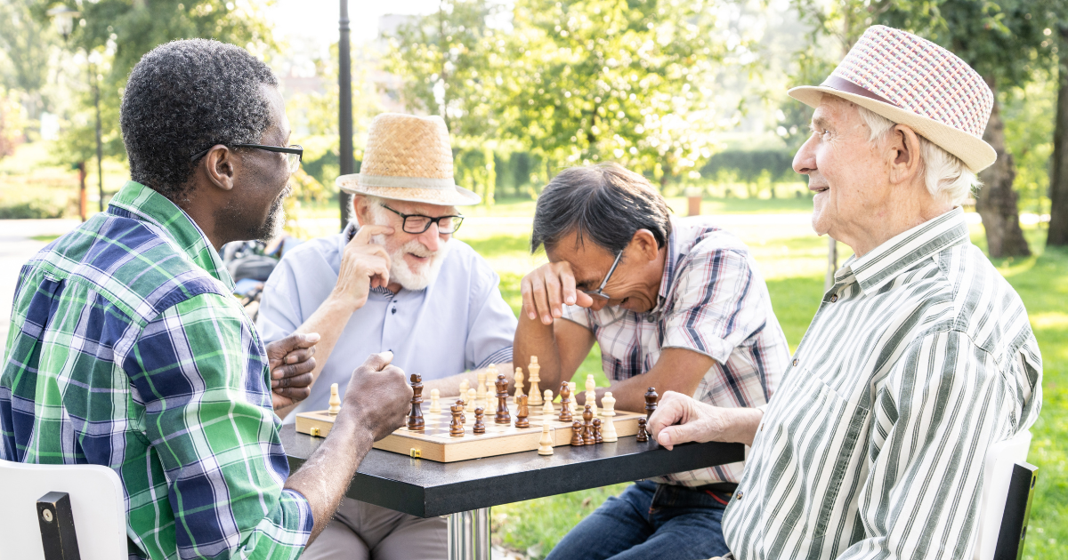 A diverse group of retired men playing chess together in a sunny park, representing low-cost hobbies, social connection, and a fulfilling retirement lifestyle on a budget leading to improved quality of life.
