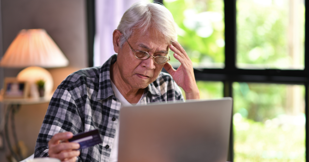 Older adult looking concerned while holding a credit card and using a laptop, representing the risk of retirement scams and common financial fraud targeting seniors.
