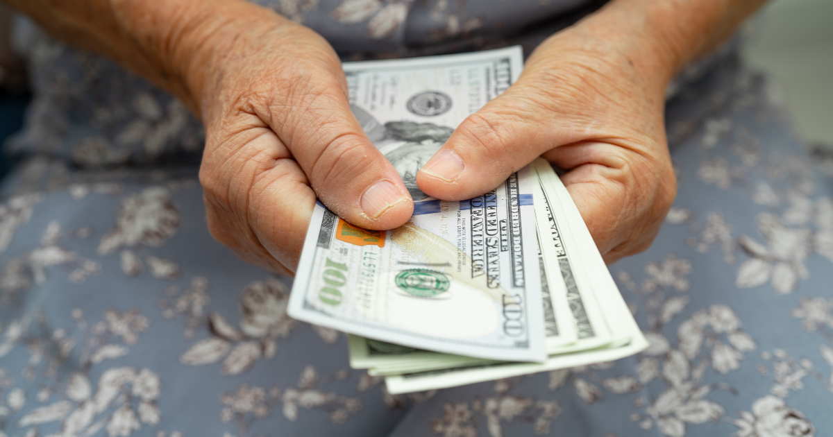 Close-up of a retiree’s hands holding hundred-dollar bills, representing the importance of sustainable retirement income planning and managing living expenses to ensure savings last for life.