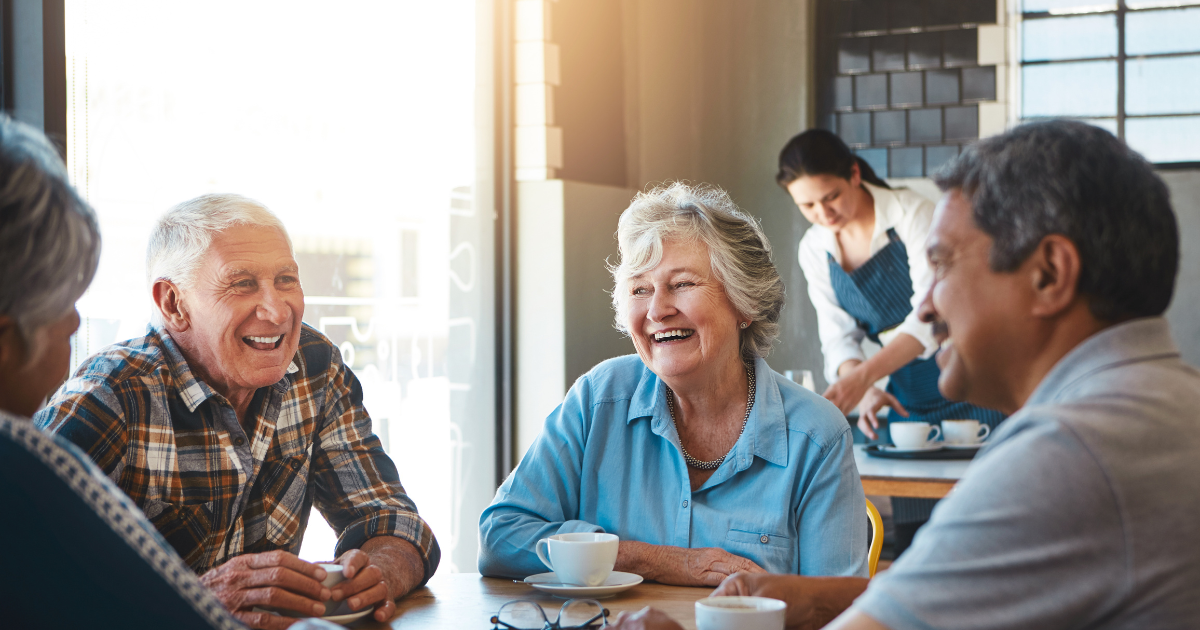 A group of happy, active pre-retirees enjoying a social gathering at a cafe, illustrating the peace of mind that comes from proactive retirement planning and a MaxAMAZING™ lifestyle.